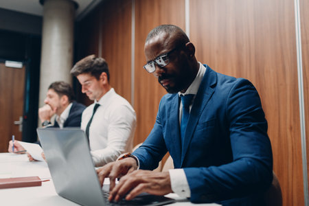 African american black man businessman sitting at table with laptop on office team people backgroundの写真素材