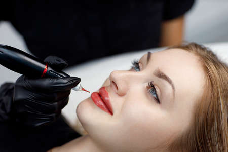 Cosmetologist applying pink pigment permanent tattoo on female lips with tatooing needle machineの写真素材