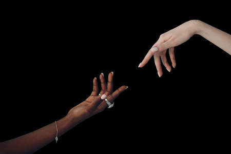 World Humanitarian Day. Caucasian white and African American black hand reaching out to each other on black background.の写真素材