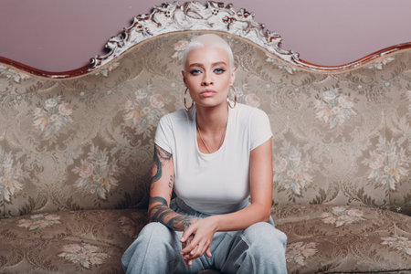 Millenial young woman with short blonde hair portrait sitting on vintage sofaの写真素材