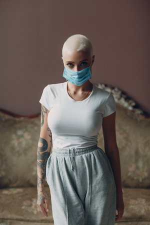 Millenial young woman in medical protective face mask with short blonde hair portrait standing indoor apartmentの写真素材
