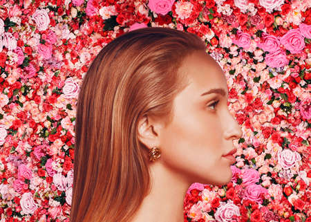 Young caucasian woman beauty profile portrait on pink rose and red roses flowers wall background. Cosmetics natural concept.の写真素材