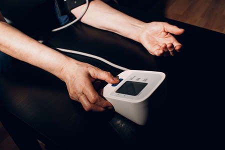 Senior woman taking measures blood pressure at home. Old hand close up. Self care of elderly health.の写真素材