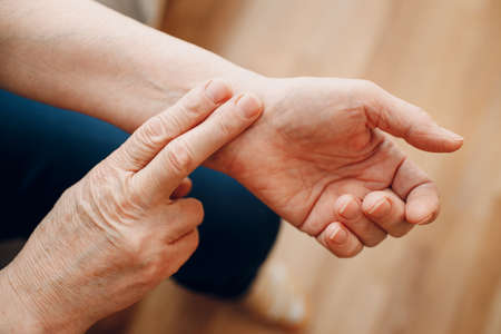 Female old hand measure taking pulse check arm pulse. Elderly woman heart health.の写真素材