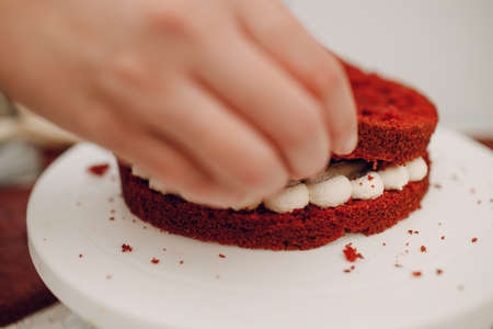 Pastry chef spreads cream and makes delicious red velvet cake. Cooking and decorating dessert.
