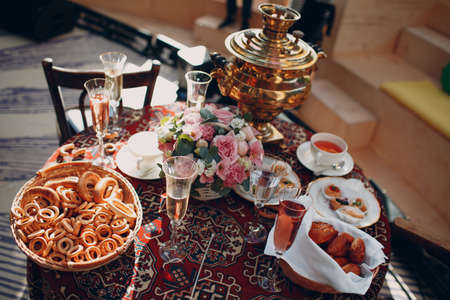 Old traditional Russian table for tea drinking with samovar, glasses of wine, flowers, pastries, bagels and bunsの写真素材