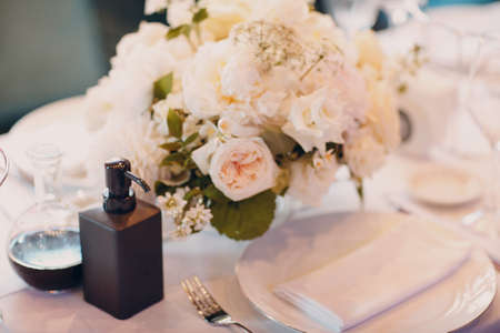 round tables in the restaurant with white tablecloths and white bouquets of flowers decor with hand sanitizer.の写真素材
