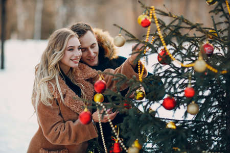 Young adult couple decorates christmas tree in winter forest. New year pine holiday party celebration conceptの写真素材