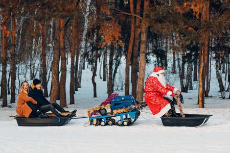 Santa claus riding on snowmobile young couple in love in the winter forest. New year party.の写真素材