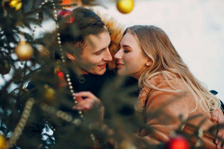Young adult couple kissing while decorates christmas tree in winter forest. New year pine holiday party celebration conceptの写真素材