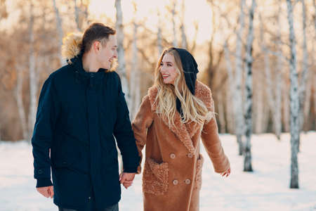 Loving young couple walking holding hands and having fun in winter forest park.の写真素材