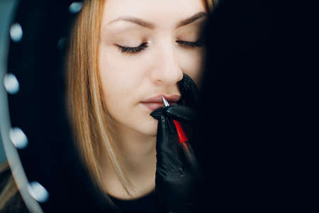 Cosmetologist applying drawing contour on lip before making lips microblading tattoo procedure. top overhead viewの写真素材