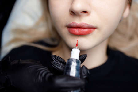 Cosmetologist master apply red permanent lips tattoo on young woman overhead viewの写真素材
