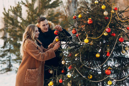 Young adult couple decorates christmas tree in winter forest. New year pine holiday party christmas celebration conceptの写真素材