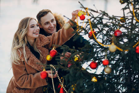 Young adult couple decorates christmas tree in winter forest. New year pine holiday party celebration concept. christmas tree decorationの写真素材