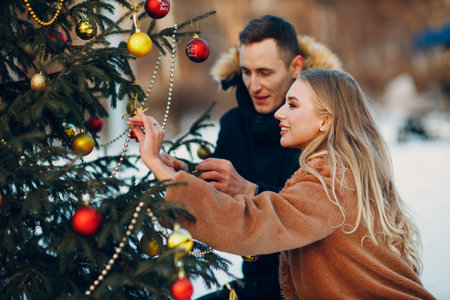 Young adult couple decorates christmas tree in winter park wood fir forest. New year pine holiday party celebration conceptの写真素材