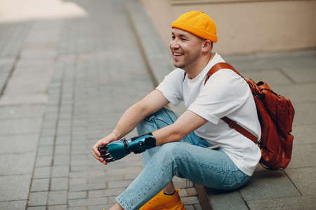 Young disabled man with artificial prosthesis hand sitting on sidewalk city street outdoor and smiling laughingの写真素材