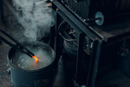 Blacksmith forges and tempering metal horseshoe in jar with water at forge.
