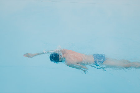 Fit swimmer male training swim in open winter swimming pool with fog. Geothermal outdoor spa health...
