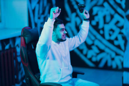 Young guy plays on game console with gamepad sitting on chair enjoying victory win.の写真素材