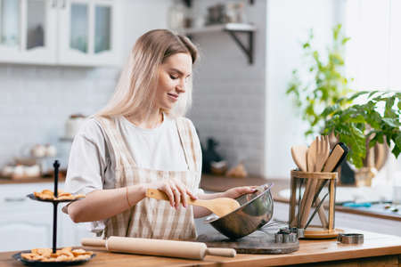 Pastry chef confectioner young caucasian woman with kitchen bowl on kitchen table. Cakes dessert...