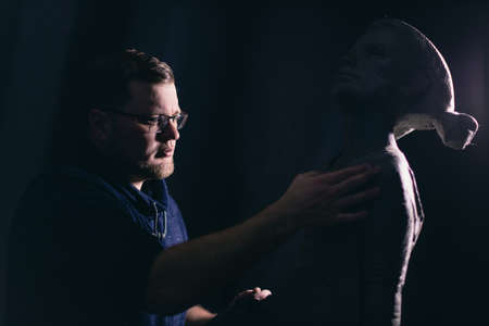Man sculptor creates sculpt bust clay human woman sculpture. Statue craft creation workshop.の写真素材