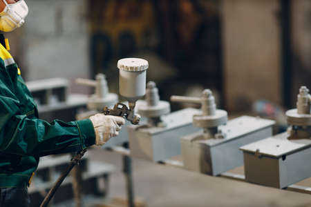 Powder primer coating of metal parts. Worker man in a protective suit sprays powder paint from gun on metal product construction at factory plant.の写真素材