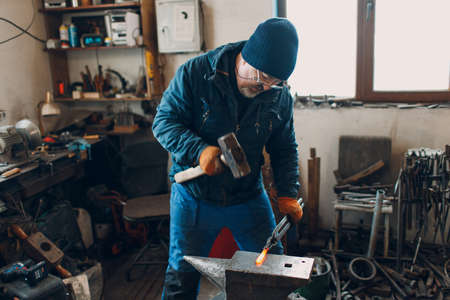 Blacksmith forges and makes metal detail with hammer and anvil at smith farrier forge.の写真素材