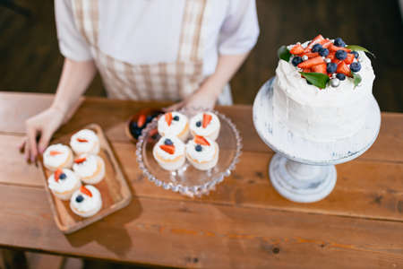 Pastry chef confectioner young caucasian woman decorate cake on kitchen table. Cakes cupcakes and sweet dessert top overhead viewの写真素材