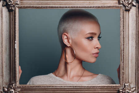 Baguette Framing Workshop Concept. Girl with short blonde hair holds gilded picture frame in hands behind her face portraitの写真素材