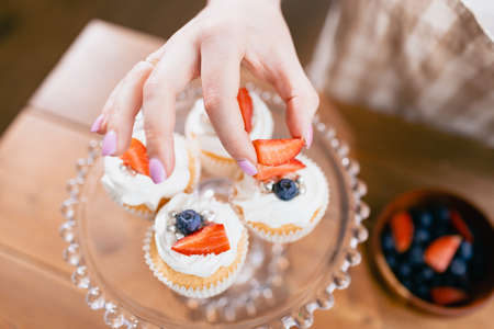 Pastry chef confectioner young caucasian woman decorate cake on kitchen table. Cakes cupcakes and sweet dessert top overhead view handの写真素材