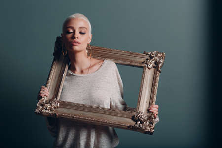Museum visual art concept. Young woman with gold picture frame baguette hold on shouldersの写真素材
