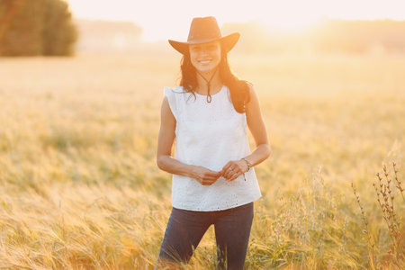 Woman farmer in cowboy hat at agricultural field on sunset.の写真素材