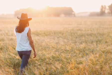 Woman farmer in cowboy hat at agricultural field on sunset.の写真素材
