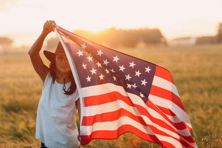 Woman farmer in the agricultural field with american flag on sunset.の写真素材