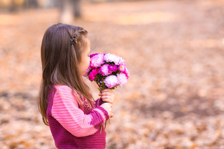 Cute little girl in autumn park with pink flower bouquet.の写真素材