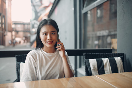 Portrait of asian woman enjoying using mobile phone sitting at outdoor cafe.の写真素材