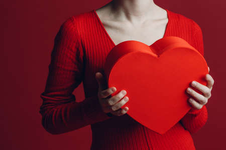 Happy young woman holding heart shaped box in Valentines day at red background.の写真素材