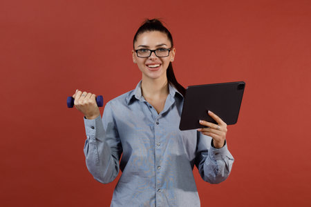 Successful young modern businesswoman in blue shirt warming up with dumbbells at office while working on tablet pc, Business, work, woman and sport fitness workout exercise conceptの写真素材