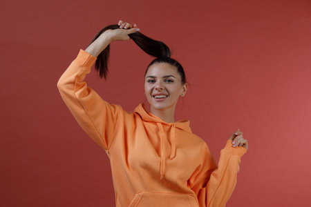 Young positive smiling woman in orange fitness sport outfit cloth suit put hold her hair in hand