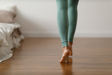 Young woman in sports leggings walks barefoot on the warm floor in the bedroom. Close-up of cropped image of barefoot girl. Underfloor heating system and laminated wood panels.の写真素材
