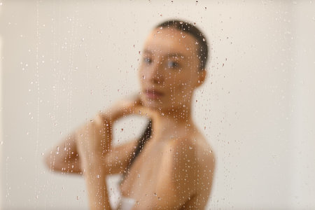 Young woman under the trickles of water in pleasure shower. Beautiful girl under the spray of water. Wet through glass drops selective focusの写真素材