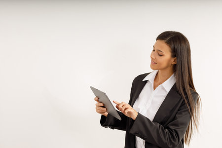 Portrait of successful business woman with tablet in her hands, dressed in white shirt and black jacket on isolated white background. Studio shot of attractive brunette girlの写真素材