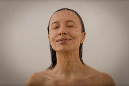 Young woman under the trickles of water in pleasure shower. Beautiful girl under the spray of water on isolated background. Wet happy faceの写真素材