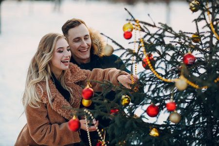 Young adult couple decorates christmas tree in winter park wood fir forest. New year pine holiday party celebration concept.の写真素材