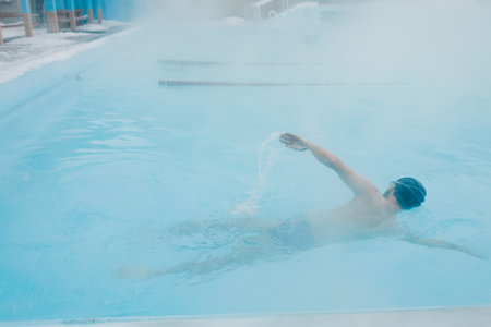 Fit swimmer male training swim in open winter swimming pool with fog. Geothermal outdoor spa health...