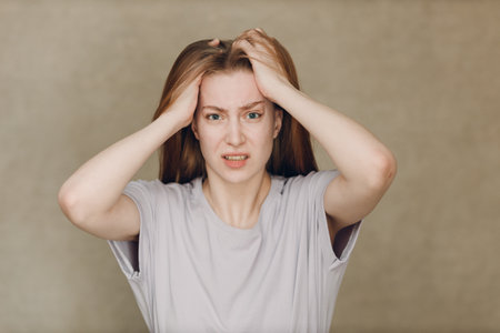 Portrait of young sad upset caucasian woman looking at camera against beige backgroundの写真素材