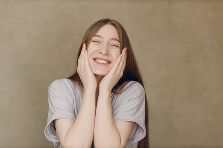 Portrait of young pretty smiling woman looking at camera against beige backgroundの写真素材
