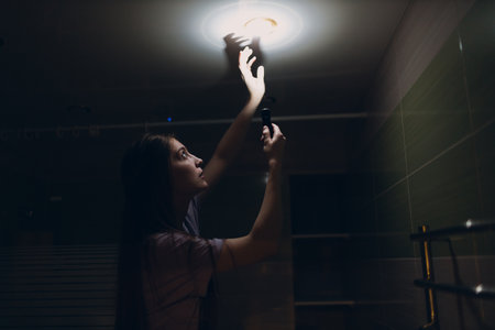 Woman young holding hand flashlight in darkness. Disconnecting home electricity and changing lamp bulbの写真素材