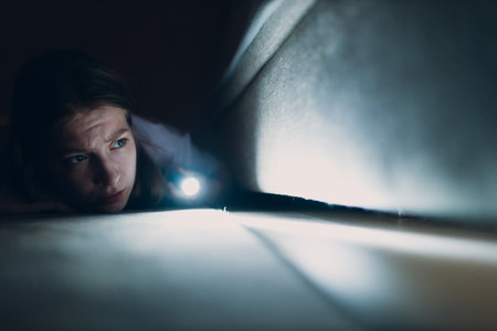Woman young holding hand flashlight looking for dirt under furnitureの写真素材